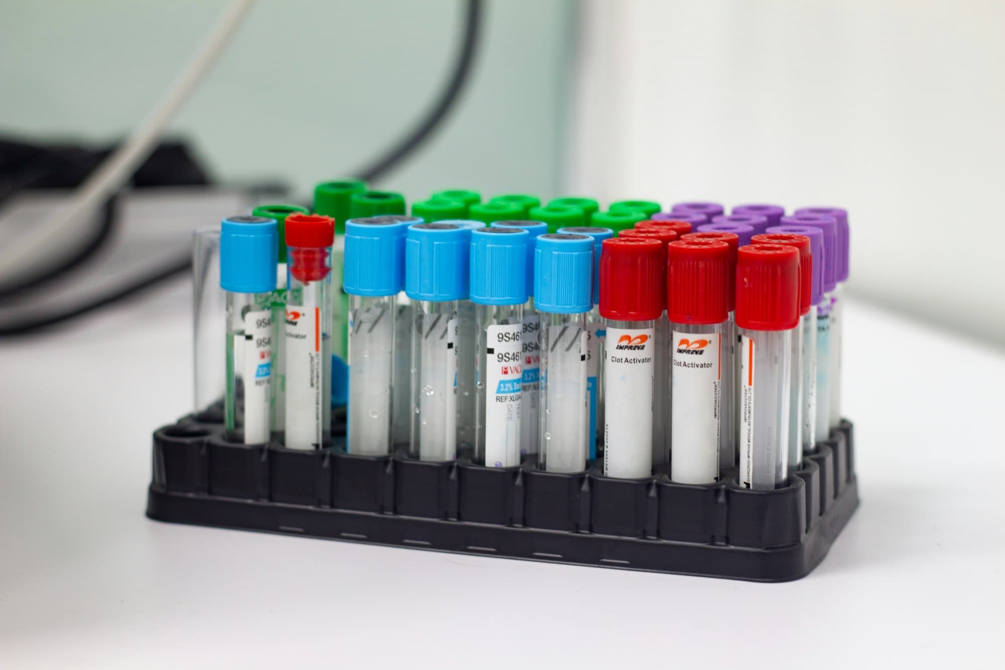 Tubos de coleta de sangue com tampas coloridas numa estante de laboratório